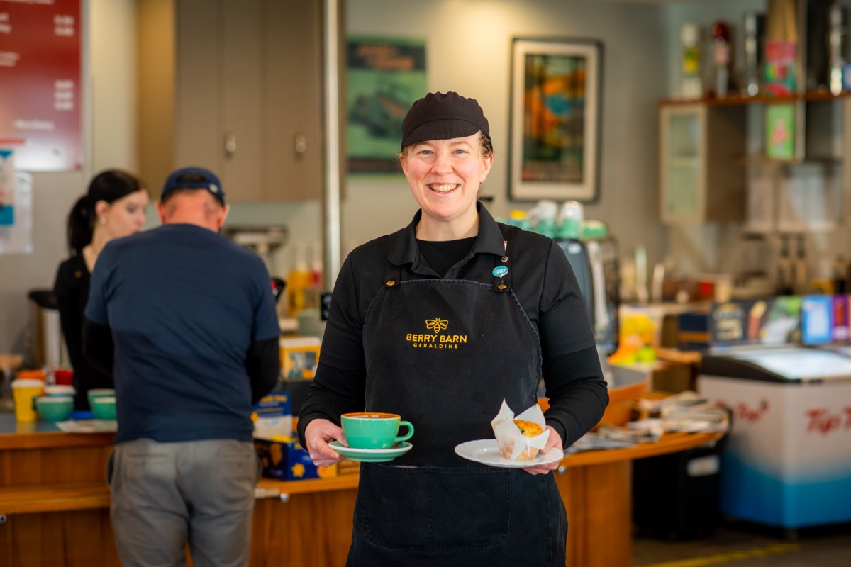 A Berry Barn staff member carrying a coffee and a slice out to a table